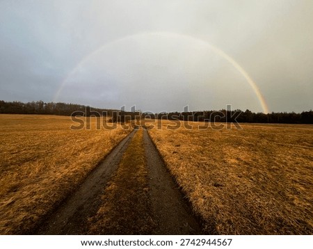 Full rainbow over rural fields and dirt road after rain