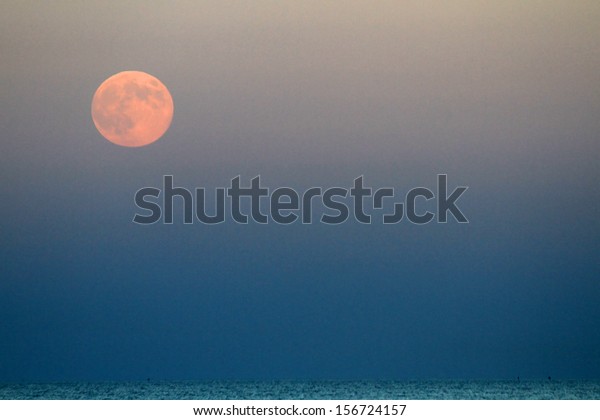 full\
Red Moon that rises above the blue sea at\
nightfall