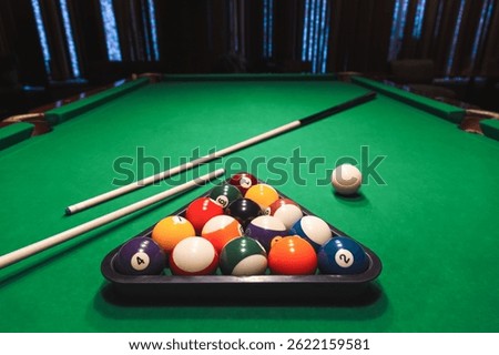 Full set of numbered pool balls arranged in a triangle rack with cue sticks on a green pool table. Bar games, cue sports
