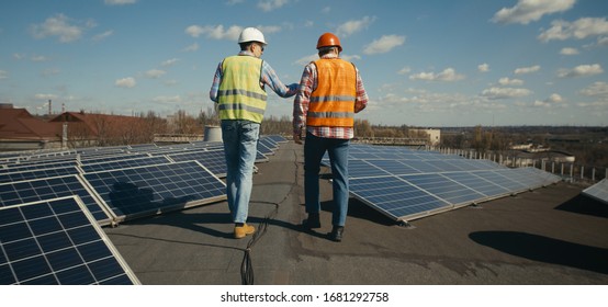 Full shot of engineer and technician discussing on flat roof between solar panels