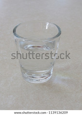 A full shot glass with clear liquid on a table 