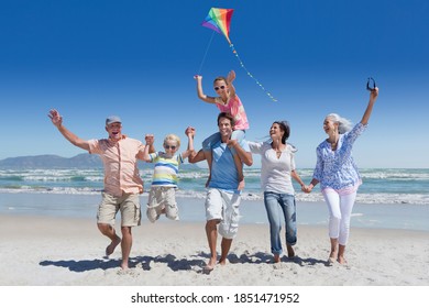 Full shot of a multi-generation family running with a kite on a sunny beach with the sea in background. - Shutterstock ID 1851471952