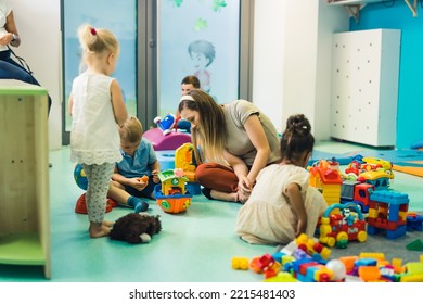 Full Shot Of A Room In The Kindergarten, Kids Playing With Their Teacher And Building Houses, Ships And Other Things. High Quality Photo