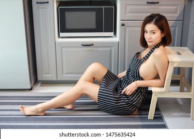 Full Shot Of Sexy And Attractive Asian Woman, Short Hair Wife In Black And White Apron, No Bra She Sitting Take A Rest While Cooking In Kitchen And Looking Camera (lifestyle Concept)