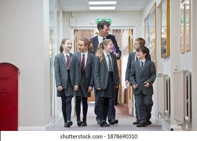 Full Shot Of A Teacher Talking To Middle School Students While Walking Through A School Corridor.