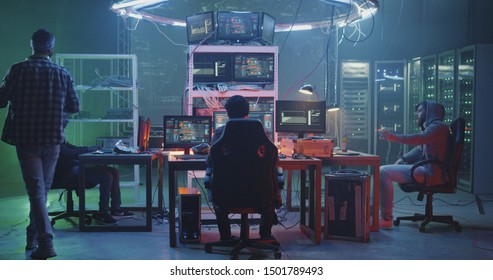 Full shot of young hackers talking while sitting at their computers in a dim basement
