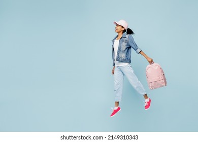 Full Side Fun Little Schoolgirl Kid Teen Girl Of African American Ethnicity 12-13 Year Old In Denim Jacket Backpack Cap Hold Exercise Books Jumping High Isolated On Pastel Plain Light Blue Background