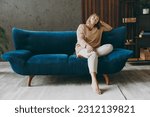 Full size body calm elderly woman 50s years old wears casual clothes sits on blue sofa prop up head close eyes dream stay at home flat rest relax spend free spare time in living room indoor grey wall