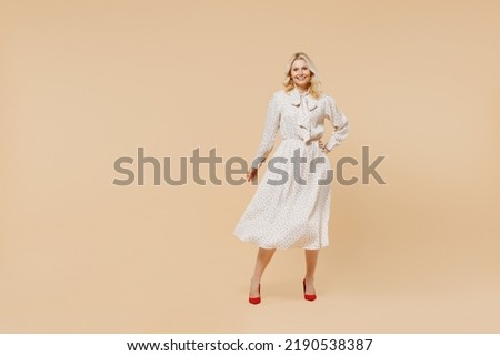 Full size body length blithesome elderly gray-haired blonde woman lady 40s years old wears pink dress hold hand on waist looking camera posing isolated on plain pastel beige background studio portrait