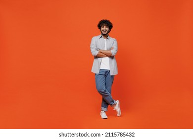 Full size body length confident happy young bearded Indian man 20s years old wears blue shirt hold hands crossed isolated on plain orange background studio portrait. People emotions lifestyle concept