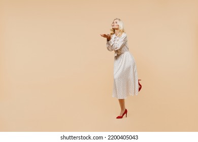 Full Size Body Length Coquette Vivid Elderly Gray-haired Blonde Woman Lady 50s Years Old Wears Pink Dress Flirt Blowing Sending Air Kiss Aside Isolated On Plain Pastel Beige Background Studio Portrait