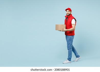 Full Size Body Length Delivery Guy Employee Man In Red Cap White T-shirt Vest Uniform Work As Dealer Courier Hold Blank Cardboard Box Isolated On Pastel Blue Color Background Studio. Service Concept