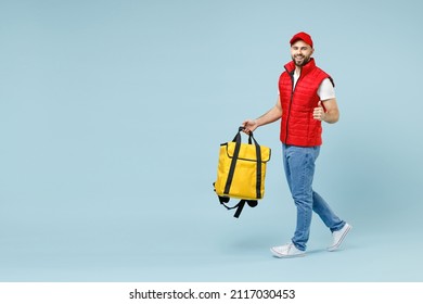 Full Size Body Length Delivery Guy Employee Man In Red Cap White T-shirt Uniform Work As Courier Hold Yellow Thermal Food Bag Backpack Isolated On Pastel Blue Color Background Studio. Service Concept