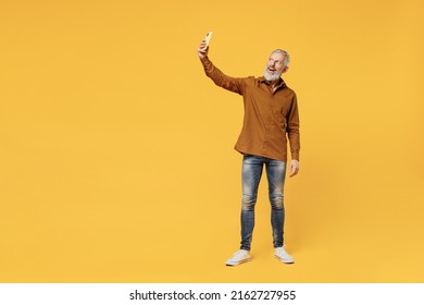 Full Size Body Length Excited Smiling Fancy Elderly Gray-haired Bearded Man 60s Years Old Wears Brown Shirt Doing Selfie Shot On Mobile Cell Phone Isolated On Plain Yellow Background Studio Portrait