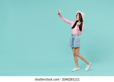 Full Size Body Length Fun Young Brunette Asian Woman 20s Wears Pink Clothes Doing Selfie Shot On Mobile Phone Showing Victory Sign Strolling Isolated On Pastel Blue Color Background Studio Portrait.