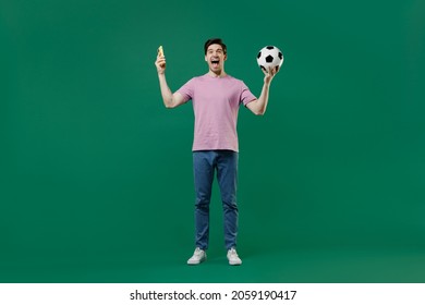 Full Size Body Length Fun Young Man Fan In Pink T-shirt Cheer Up Football Sport Team Hold Hand Soccer Ball Mobile Cell Phone Watch Tv Live Stream Scream Isolated On Dark Green Color Background Studio