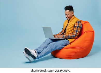 Full size body length fun young black man 20s years old wears yellow waistcoat shirt sit in bag chair hold use work on laptop pc computer isolated on plain pastel light blue background studio portrait - Shutterstock ID 2085990391