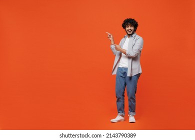 Full Size Body Length Fun Young Bearded Indian Man 20s Years Old Wears Blue Shirt Pointing Index Fingers Aside On Workspace Area Copy Space Mock Up Isolated On Plain Orange Background Studio Portrait