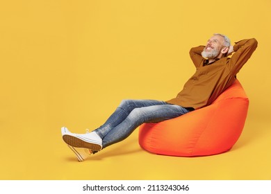 Full Size Body Length Happy Elderly Gray-haired Bearded Man 40s Years Old Wears Brown Shirt Hands Folded Under Head Have Rest Relax Sit In Bag Chair Isolated On Plain Yellow Background Studio Portrait