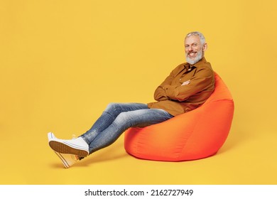 Full size body length happy elderly gray-haired bearded man 60s years old wears brown shirt sit in bag chair look camera smiling keep hands crossed isolated on plain yellow background studio portrait - Shutterstock ID 2162727949