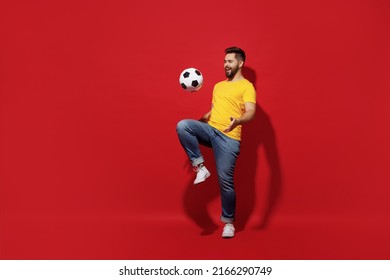 Full size body length overjoyed excited jubilant fun young bearded man football fan in yellow t-shirt juggling soccer ball isolated on plain dark red background studio portrait. Sport leisure concept