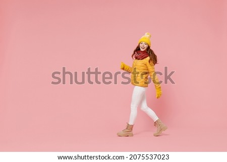 Full size body length overjoyed excited young woman 20s years old wears yellow jacket hat mittens looking camera walking stepping pacing isolated on plain pastel light pink background studio portrait