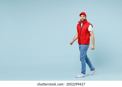 Full size body length professional delivery guy employee man in red cap white T-shirt vest uniform workwear work dealer courier walk go isolated on pastel blue color background studio. Service concept