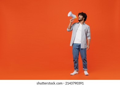 Full size body length promoter young bearded Indian man 20s years old wears blue shirt hold scream in megaphone announces discounts sale Hurry up isolated on plain orange background studio portrait