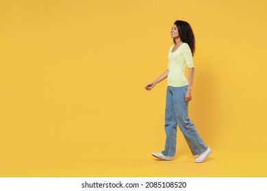 Full Size Body Length Side View Profile Smiling Happy African American Young Woman 20s Wears Green Shirt Move Go Step Isolated On Yellow Background Studio Portrait. People Emotions Lifestyle Concept.