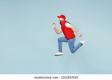 Full size body length side view delivery guy employee man in red cap white T-shirt vest uniform work as dealer courier jump run go walk isolated on pastel blue color background studio. Service concept