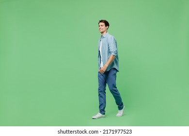 Full size body length side view blithesome charismatic stunning delight young brunet man 20s years old wears blue shirt looking aside strolling pace isolated on plain green background studio portrait