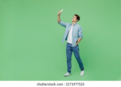 Full Size Body Length Side View Young Brunet Man 20s Years Old Wears Blue Shirt Doing Selfie Shot On Mobile Cell Phone Post Photo On Social Network Isolated On Plain Green Background Studio Portrait