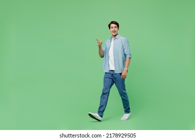 Full Size Body Length Side View Fun Young Brunet Man 20s Years Old Wears Blue Shirt Pointing Index Finger Aside On Workspace Area Copy Space Mock Up Isolated On Plain Green Background Studio Portrait