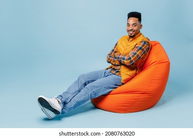 Full Size Body Length Smiling Young Black Man 20s Years Old Wears Yellow Waistcoat Shirt Sit In Bag Chair Hold Hands Crossed Look Camera Isolated On Plain Pastel Light Blue Background Studio Portrait