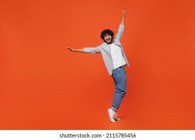 Full size body length smiling young bearded Indian man 20s years old wears blue shirt standing on toes dancing lean back have fun spreading hands isolated on plain orange background studio portrait - Shutterstock ID 2115785456
