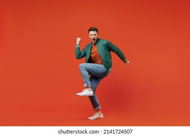 Full Size Body Length Smiling Vivid Fun Young Brunet Man 20s Wears Red T-shirt Green Jacket Doing Winner Gesture Celebrating Clenching Fists Say Yes Isolated On Plain Orange Background Studio Portrait