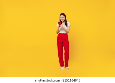 Full size body length smiling fun young girl woman of Asian ethnicity 20s years old wears casual clothes hold in hand use mobile cell phone send sms isolated on plain yellow background studio portrait