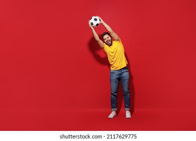 Full Size Body Length Vivid Young Bearded Man Football Fan In Yellow T-shirt Support Favorite Team Hold Catch Soccer Ball Isolated On Plain Dark Red Background Studio Portrait. Sport Leisure Concept