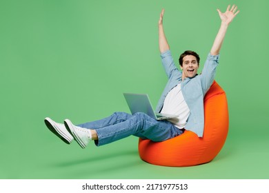 Full size body length vivid young brunet man 20s years old wears blue shirt sit in bag chair hold use work on laptop pc computer raise hands palms up isolated on plain green background studio portrait - Shutterstock ID 2171977513