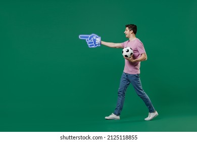 Full size body length young fun man fan wear basic pink t-shirt cheer up support football sport team hold in hand soccer ball watch tv live stream scream isolated on dark green color background studio