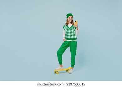 Full size body length young brunette girl teen student wears checkered green vest hold in hand use mobile cell phone stand on skateboard isolated on plain pastel light blue background studio portrait - Shutterstock ID 2137503815
