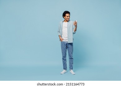 Full size body length young black curly man 20s years old wears white shirt hold in hand use mobile cell phone typing browsing chatting isolated on plain pastel light blue background studio portrait