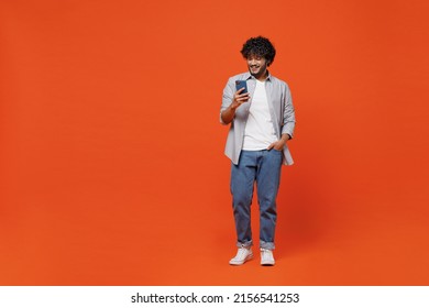 Full Size Body Length Young Bearded Indian Man 20s Years Old Wears Blue Shirt Hold In Hand Use Mobile Cell Phone Typing Browsing Chatting Send Sms Isolated On Plain Orange Background Studio Portrait