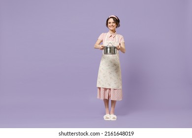 Full Size Body Length Young Un Housewife Housekeeper Chef Cook Baker Woman In Pink Apron Hold Soup Stainless Pan Saucepan Look Camera Isolated On Pastel Violet Background Cooking Food Process Concept