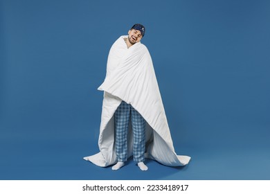 Full size body length young fun man 20s wear pajamas jam sleep mask resting relax at home wrap cover with blanket duvet look camera isolated on dark blue background Good mood night bedtime concept.