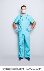 Full Size Body Portrait Of Attractive Handsome Man In Sterile Mask And Blue Lab Uniform, Holding Arms On Waist, Looking At Camera Isolated On Grey Background