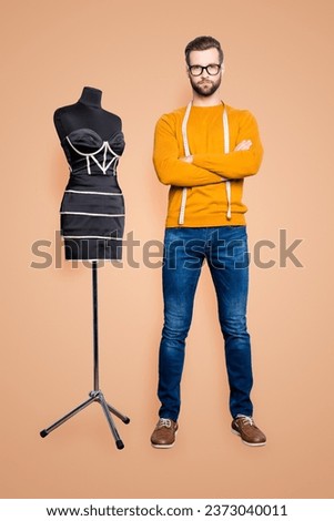 Full size body portrait of virile harsh dressmaker with centimeter on neck in pullover, jeans holding arms crossed, looking at camera isolated on grey background