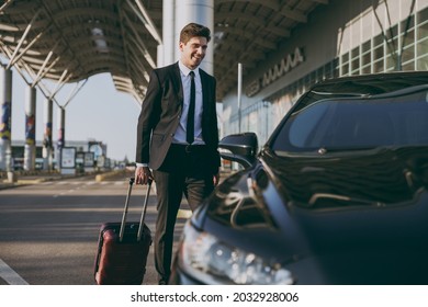 Full size bottom view young traveler businessman young man in black dinner suit going walk outside at international airport terminal with suitcase to car booking taxi Air flight business trip concept.