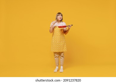 Full Size Elderly Satisfied Fun Happy Housekeeper Housewife Woman 50s In Orange Apron Hold Empty Frying Pan Cook Sniff Isolated Plain On Yellow Background Studio. People Household Lifestyle Concept