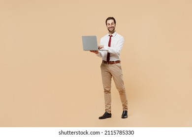 Full Size Fun Smiling Young Successful Employee Business Man Corporate Lawyer 20s Wear White Shirt Red Tie Glasses Work In Office Hold Use Laptop Pc Computer Isolated On Plain Beige Background Studio